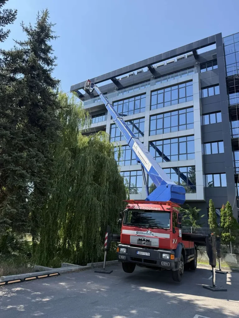 Автовишка с изцяло вдигната стрела до остъклена офис сграда